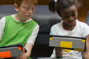 Two children sitting on a couch using electronic devices, representing technology use in modern educational environments