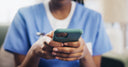 Healthcare worker in medical scrubs using a smartphone to manage patient information or communicate in a clinical setting