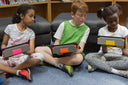 Three children using tablets with colorful Nutkase protective cases with kickstands in classroom setting
