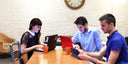  Three individuals collaborating with laptops and tablets around a table in a casual workspace environment, showcasing NutKase tech protection in action