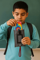 Child holding a tie-dye cased iPhone with a NutKase phone pouch in front of a green chalkboard background, ideally  a classroom environment