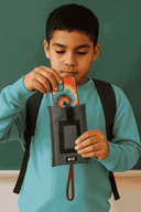 Child holding a tie-dye cased iPhone with a NutKase phone pouch in front of a green chalkboard background, ideally  a classroom environment